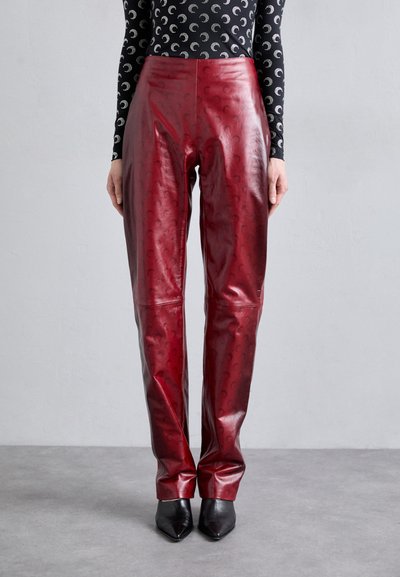 Rode leren broek met een glanzende afwerking, voorzien van een subtiel patroon. Gecombineerd met zwarte pumps met spitse neus en een nauwsluitende top met lange mouwen.