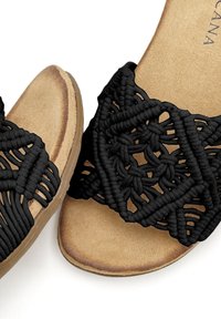 Sandali neri intrecciati con un design in macramè testurizzato, una suola beige imbottita e un profilo piatto per il massimo comfort.