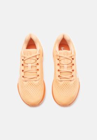 Ténis de desporto laranja claro com parte superior em malha respirável, atacadores planos, palmilha acolchoada e um logo da Nike branco na lateral.