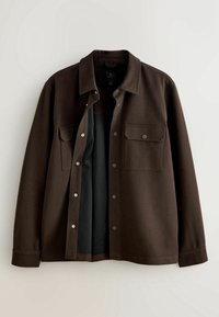 Veste marron foncé boutonnée avec manches longues, deux poches avant à rabat et devant partiellement ouvert montrant une doublure intérieure noire.