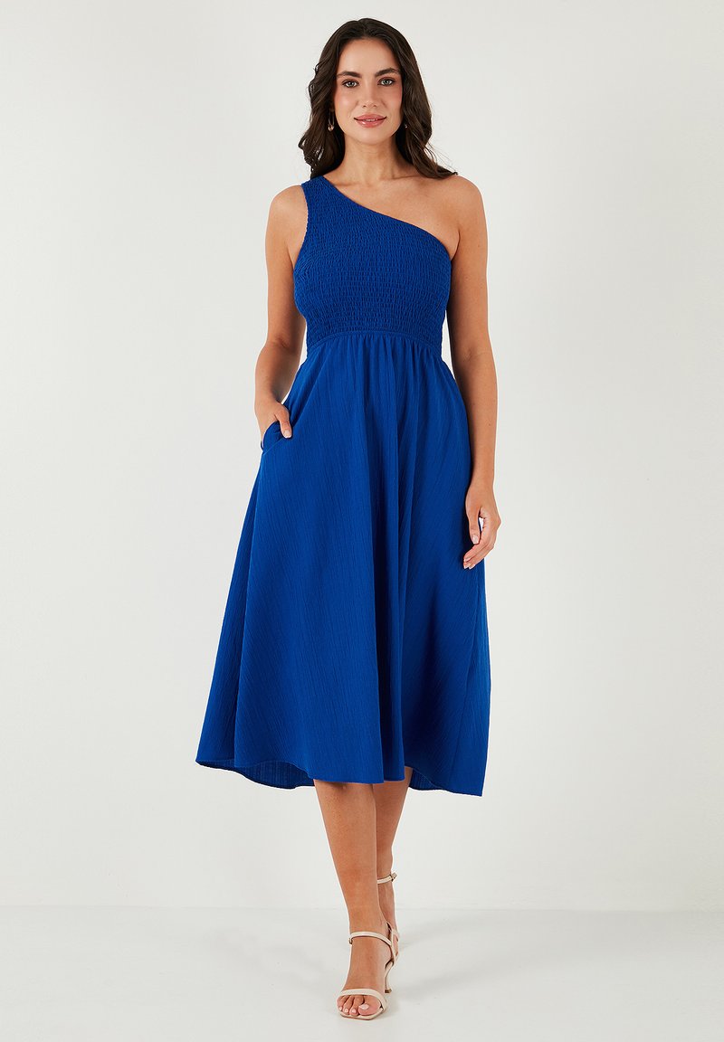 One-shoulder blue dress with a smocked bodice and flowing skirt. Features pockets and a midi length. Smooth fabric texture.
