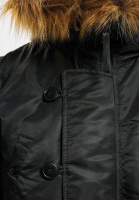 Schwarze Steppjacke mit einer Kapuze aus braunem Kunstfell, glatter Textur, auffälligen schwarzen Knöpfen und einer Brusttasche als Detail.