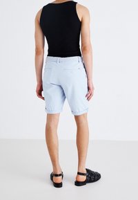 Shorts bleu clair avec revers, poches arrière et une ceinture tissée blanche. Portés avec un débardeur noir et des sandales tissées noires.