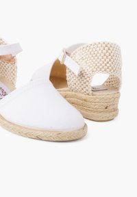 Espadrilles en toile blanche avec un dos tissé, dotées d'une semelle en jute texturée et d'une petite sangle à boucle réglable.