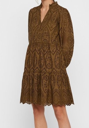 Robe marron mi-longue avec broderie anglaise, manches longues, un ourlet volanté et un col en V, portée par une personne avec les jambes visibles.
