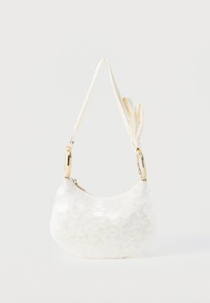 Sac à bandoulière blanc texturé avec une fine bandoulière, des anneaux dorés, une fermeture éclair et un pompon noué, sur un fond uni.
