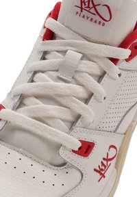 Valged sneakers tekstureeritud nahkupperiga, punaste aktsentide ja perforatsiooni detailidega. Omab lamedaid valgeid kingapaelu ja silmapaistvat logo keeles.