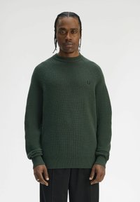 Maglione verde scuro a coste con scollo rotondo, caratterizzato da maniche lunghe e una vestibilità rilassata. Piccolo logo sul petto, texture morbida.