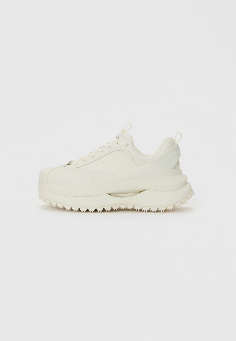 Sapatilhas grossas de cor off-white com sola espessa e em camadas, alças na lingueta e no calcanhar, e sola texturizada para melhor aderência.