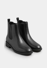 Mustat Chelsea-kengät, jotka on valmistettu sileästä nahasta, joissa on joustavat sivupaneelit, pyöristetyt varpaat ja matala lohkokorko. Huomattavaa ompelua ympärillä pohjaa.