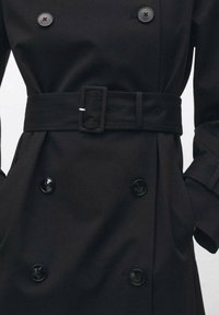 Palton negru cu un design cu două randuri de nasturi, nasturi mari negri, o curea asortată lata și mâneci structurate. Textură de țesătură netedă.