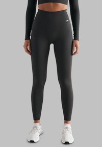 Ribbe svarte tights med høy midje og ankellang design, parret med hvite joggesko på en grå bakgrunn.
