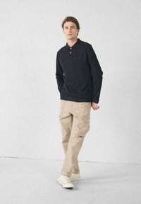 Polo a maniche lunghe blu navy con colletto a tre bottoni, abbinato a pantaloni cargo beige con tasche. Sneakers bianche con accenti rossi.
