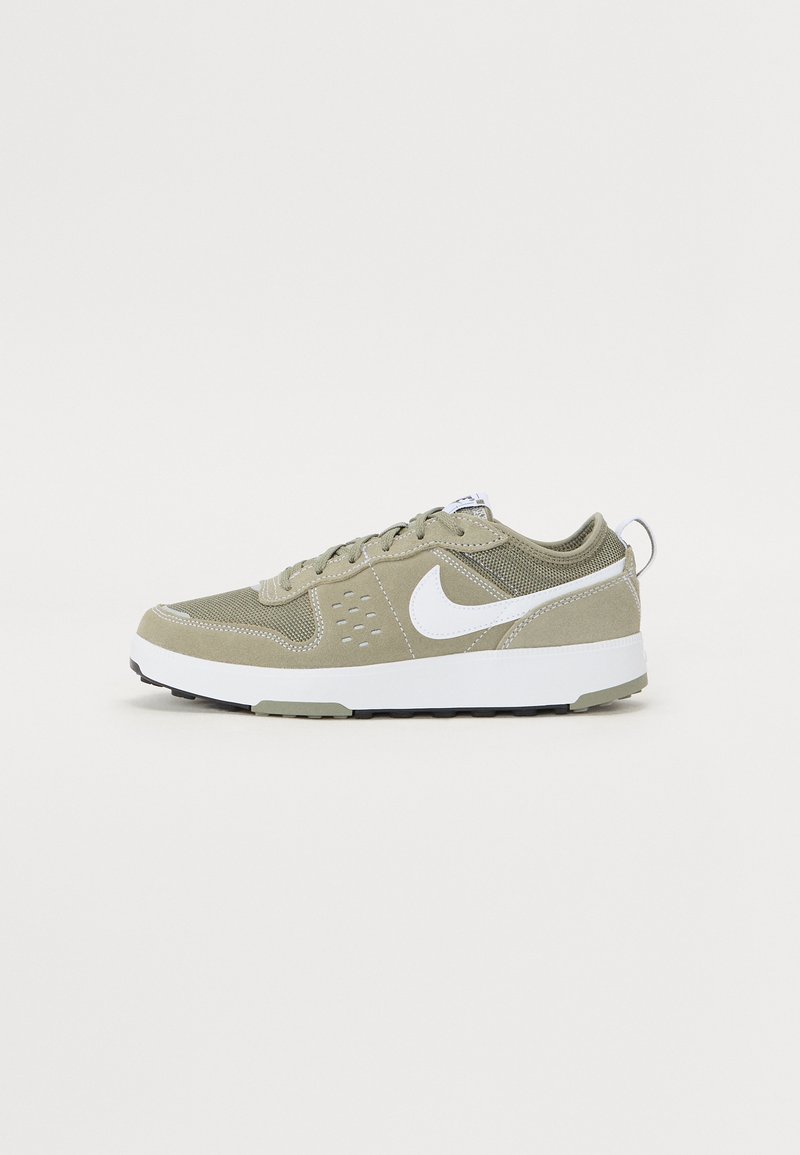 Sapatilha verde-oliva com material em malha e camurça, swoosh branco da Nike, biqueira arredondada, sola branca plana e atacadores.