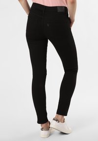 Vaqueros negros ajustados con una textura suave, que cuentan con una cintura alta, bolsillos traseros y una etiqueta de marca. Combinados con zapatillas blancas con un acento de patrón.