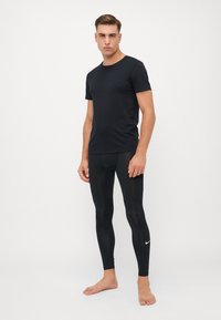 Schwarzes Crew-Neck-T-Shirt, kombiniert mit schwarzen, eng anliegenden Leggings. Die Leggings haben ein kleines weißes Nike-Logo am Unterschenkel.