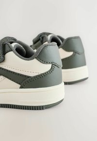 Zielono-białe sneakersy z teksturowanym materiałem i niskim wykończeniem są pokazane z tyłu na neutralnym tle.