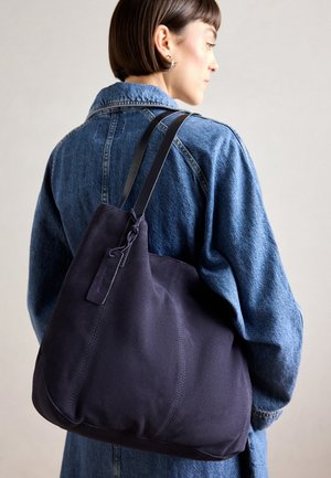 Marine canvas schoudertas met een zachte, gestructureerde vorm, voorzien van een zwarte strap, gestikte details en een klein merketiket.