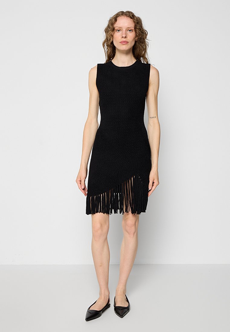 Schwarzes ärmelloses Kleid aus strukturiertem Stoff mit asymmetrischem Saum, der am unteren Rand mit Fransen verziert ist. Figurbetonte Silhouette ohne sichtbare Verschlüsse.