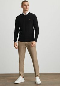 Sort striktrøje med V-hals, prydet med et orange logo. Sammen med lyse beige slim-fit chinos og hvide sneakers. Flad, afslappet design.