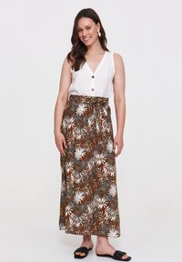 Biała bezrękawnikowa bluzka z guzikami, w połączeniu z brązową, wzorzystą maxi spódnicą z białymi kwiatowymi wzorami. Całość dopełniają czarne płaskie sandały.
