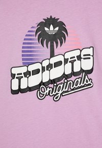 Violet marškinėliai su grafiniu atspaudu, vaizduojančiu palmę ir „ADIDAS Originals“ drąsiais juodais ir baltais rašmenimis švelniame fone.