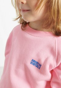 Felpa rosa realizzata in morbido cotone, con un logo blu "AMERICAN VINTAGE" sul petto e un colletto girocollo classico.