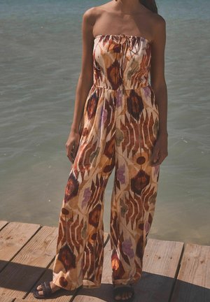 Combinaison sans bretelles à motifs avec une ceinture élastique. Le tissu présente des couleurs terreuses avec des formes abstraites dans des tons orange, marron et violet.