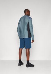 Long-sleeve teal athletic top with black side panels, paired with blue shorts. All clothing is designed for activewear, featuring a sleek fit.