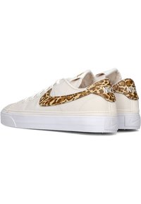 Zapatillas de lona blancas con un acento de estampado de leopardo marrón en el talón. Suela plana de goma blanca, cordones redondos y un diseño clásico.