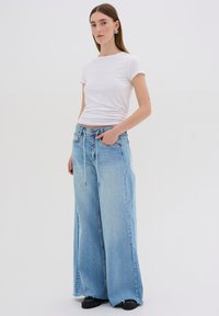 Light blue wide-leg jeans with a frayed hem, paired with a fitted white t-shirt. Features front pockets and drawstring waist accents.