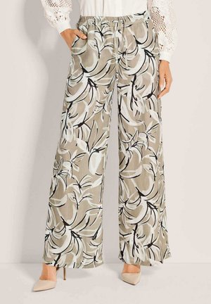 Beige Hosen mit weitem Bein und schwarz-weißem abstraktem Blumenmuster, kombiniert mit einer weißen Bluse und beigen spitzen High Heels.