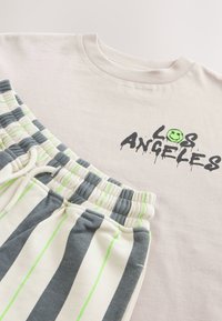 Hellgraues T-Shirt mit schwarzem "LOS ANGELES"-Aufdruck und einem grünen Smiley-Gesicht. Ein Paar gestreifte Shorts in Creme, Grau und Limettengrün.