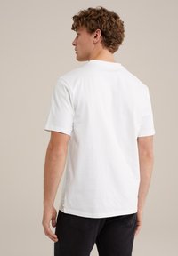 Vit bomullströja med korta ärmar, rundad halsringning och etikett vid den nedre sömmen, visad bakifrån mot en neutral bakgrund.