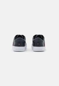 Sneakers in pelle nera con suola bianca. Presentano dettagli rossi e blu, una texture liscia e un contrafforte del tallone con il logo "HILFIGER".