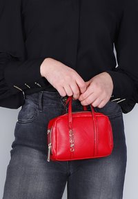 Rode leren handtas met een rechthoekige vorm, twee korte handvatten, een zilveren rits en opvallende branding aan de voorkant.