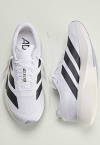 White running shoes with black stripes, one shoe facing up showing "ADIZERO" label, and the other shoe on its side with untied laces.
