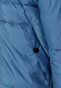 Ljusblå puffjacka med quiltade sektioner, en slät yta och en svart knappstängning vid sömmen.