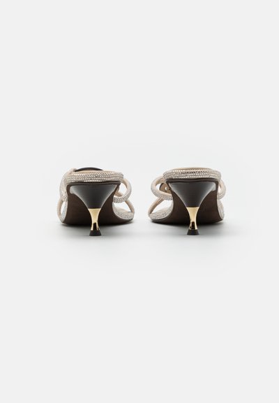 Chaussures à talons hauts beige avec une semelle en cuir lisse, des brides perlées délicates et un accent doré sur le talon. Design classique à dos ouvert.