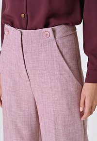 Pantaloni rosa con texture e vita aderente, dotati di due tasche frontali, chiusura con cerniera e due bottoni rosa. Abbinate a un top borgogna.