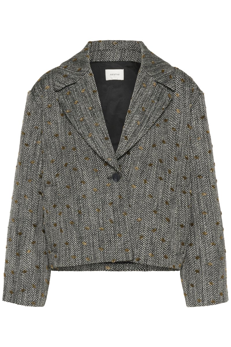 Afskåret blazer i hundtandmønster; sort og hvid med guldprikker. Har spidse klapper og en enkelt knaplukning. Tekstureret stof.