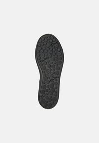 Black rubber shoe sole with circular patterns and "Camper" branding. Features textured grip areas and a smooth, rounded heel.