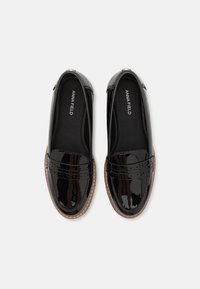 Mocassins en cuir verni noir avec une finition lisse, dotés de coutures décoratives et d'une semelle marron clair. L'intérieur possède un doux revêtement noir.