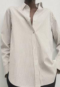 Långärmad skjorta med knappar i vertikala beige och bruna ränder, lättviktsmaterial, avslappnad passform och en något öppen krage.