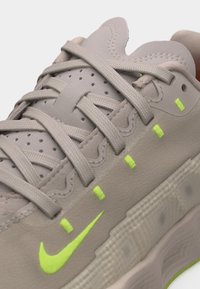 Μπεζ αθλητικό παπούτσι με υφασμένα κορδόνια, διάτρητη γλώσσα, νέον πράσινο λογότυπο Nike και μικρές ραφές νέον πράσινου χρώματος στην πλαϊνή επιφάνεια.