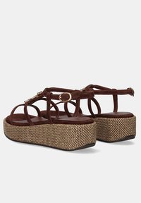 Sandalias plataforma de ante marrón con suelas con cuña texturizadas tejidas y correas para el tobillo con hebillas doradas y pequeñas cuentas decorativas.