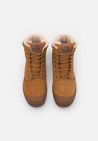 Bottes en suede marron avec un intérieur rembourré, un bout arrondi et une semelle en caoutchouc marron. Présente des œillets en métal et un patch logo sur la languette.