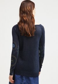 Marineblauer Strickpullover mit langen Ärmeln, der farbenfrohe Blumenmuster an den Ärmeln aufweist. Texturierter Stoff mit leichtem Glanz. Gerippter Saum.