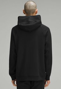 Sudadera negra con capucha, de corte relajado, mangas raglán y una textura suave. Sin patrones visibles ni detalles de hardware.