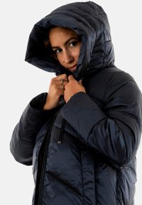 Chaqueta de plumas navy con textura brillante, cuello alto y capucha con cordón. Presenta cierre de cremallera y detalles cosidos en la tela.